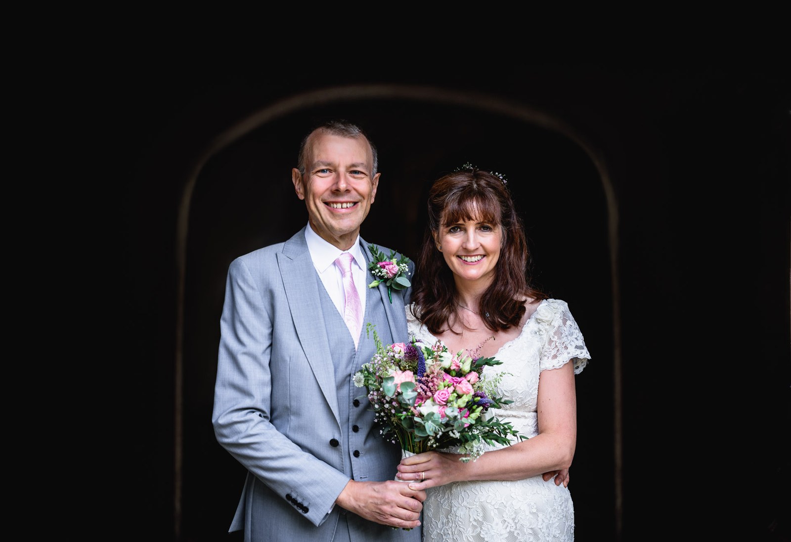 The couple smiling together, framed in a shadowed stone doorway