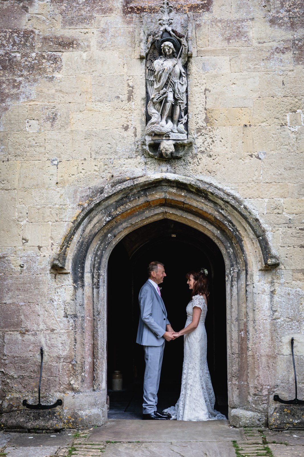 The couple holding hands in an arched stone doorway with a carved statue niche above