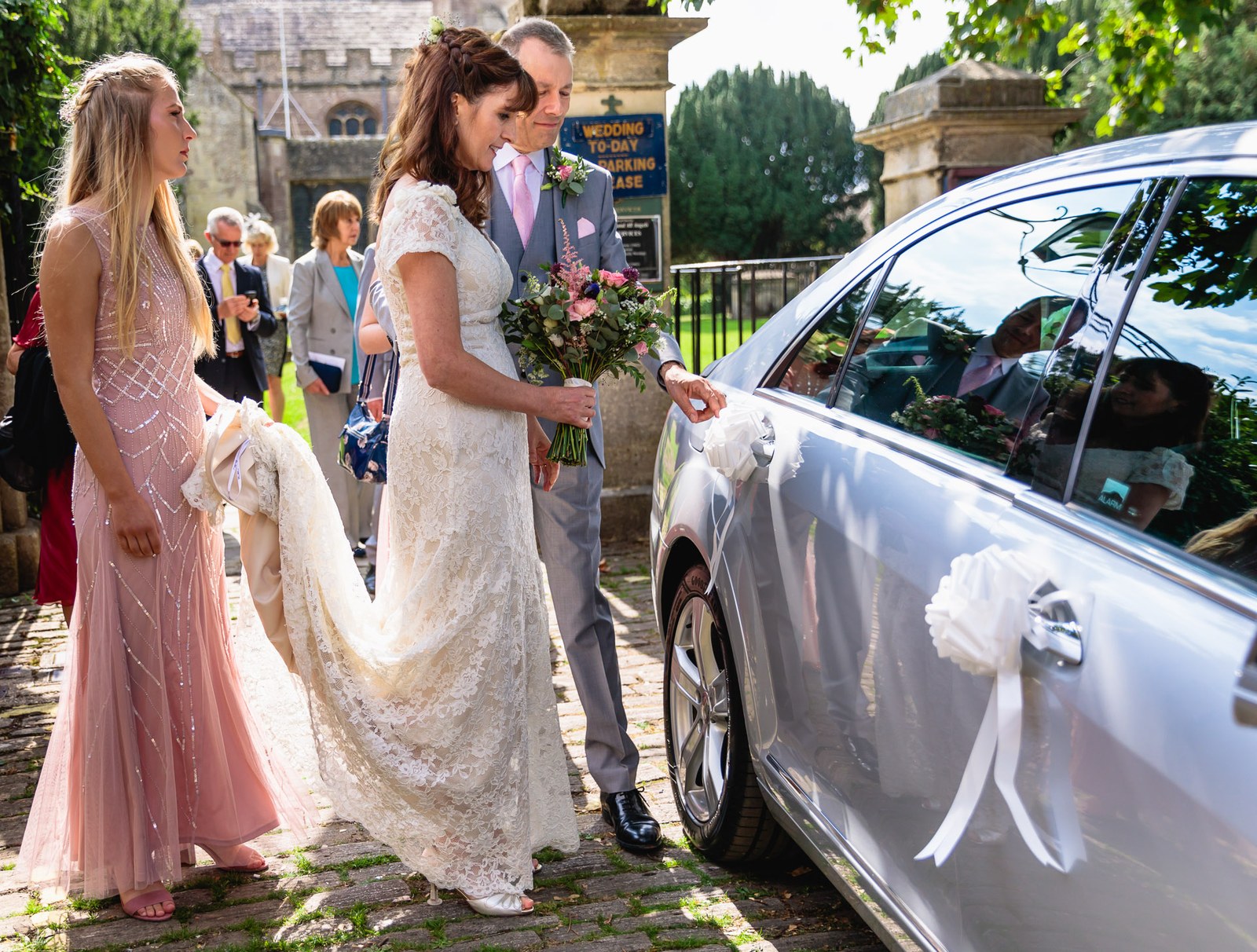Bride and bridesmaid walking to the ribbon-decorated silver wedding car
