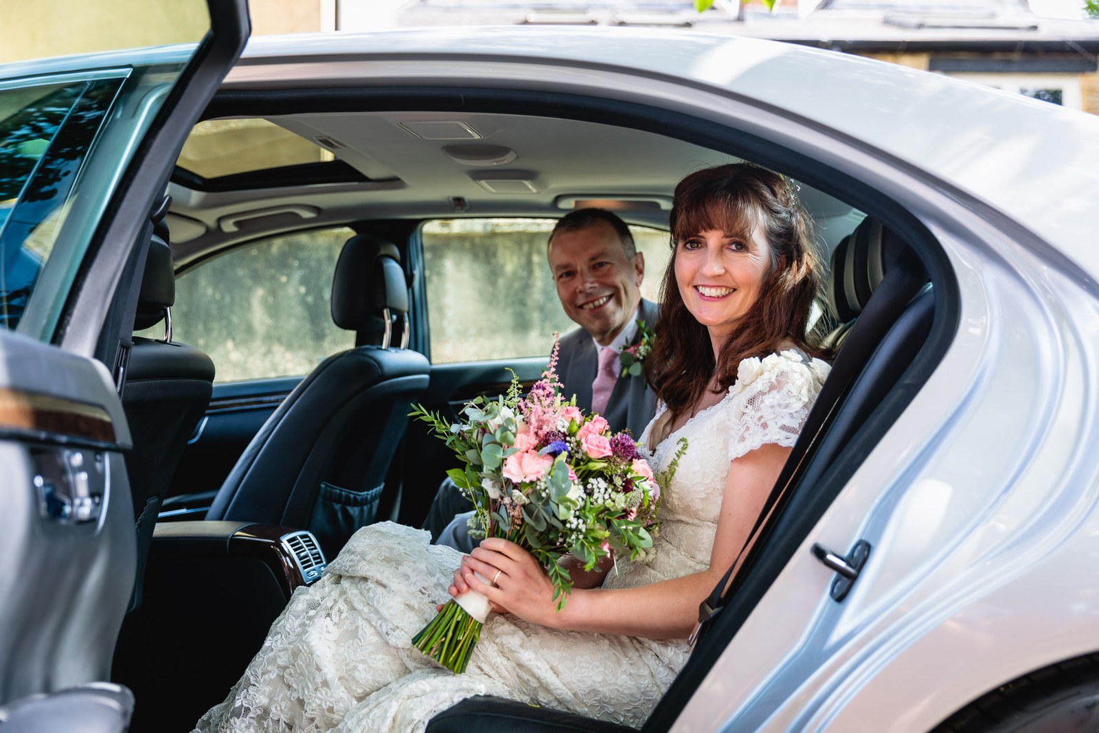 The couple at the open door of the wedding car, bride holding her bouquet