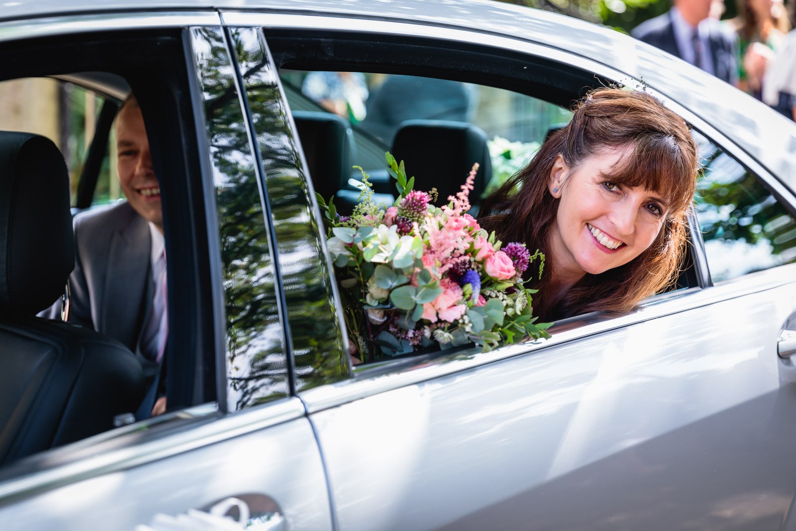 Bride leaning from the car window with her bouquet, the groom beside her