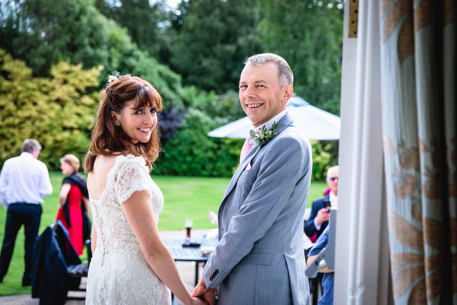 Bride and groom turning to smile, hand in hand on the garden terrace