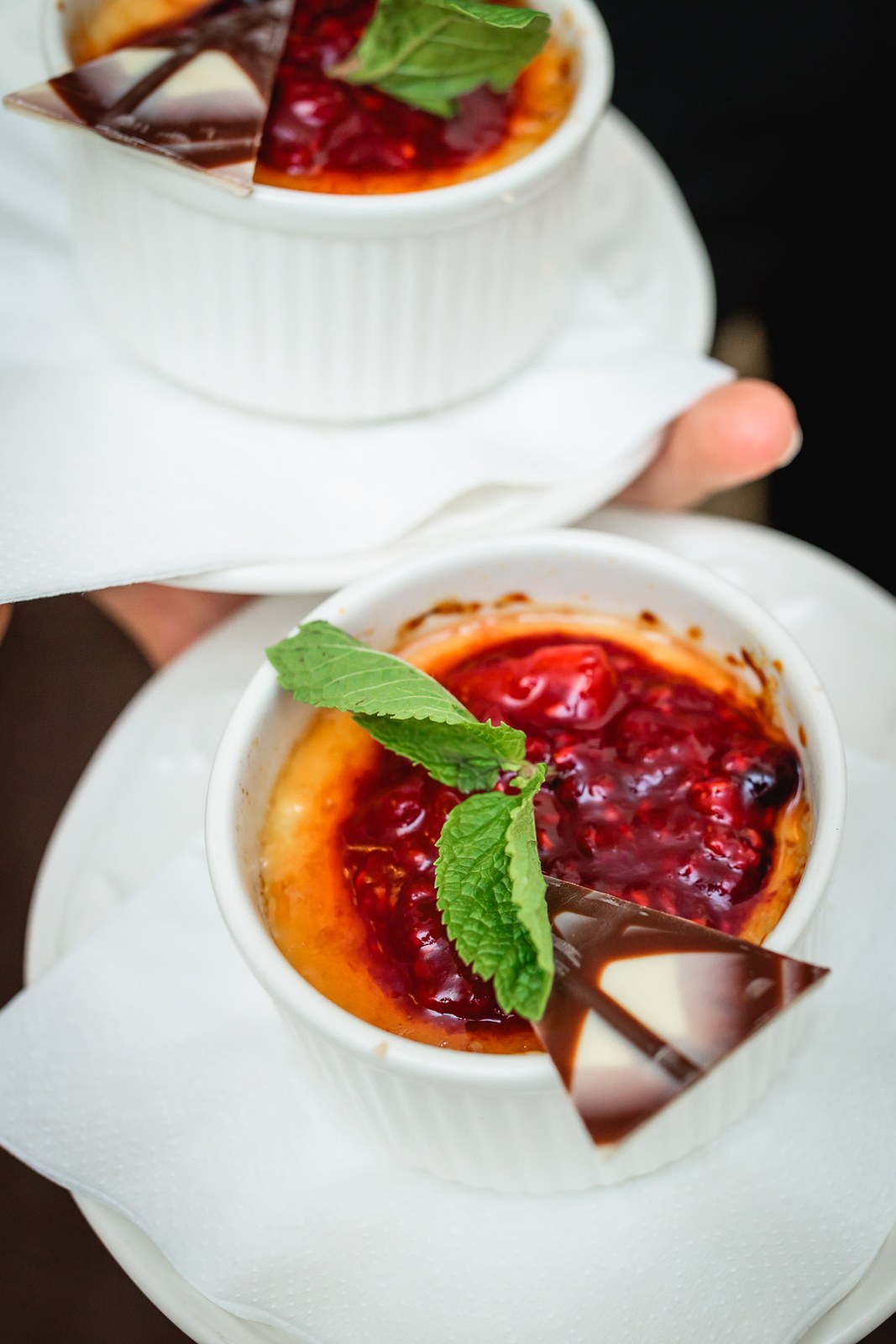 Close-up of berry creme brulee desserts garnished with mint in white ramekins