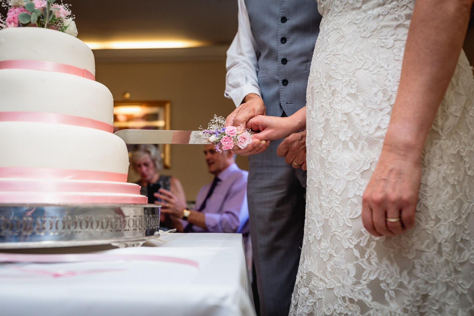 Close-up of the couple's hands cutting their tiered wedding cake