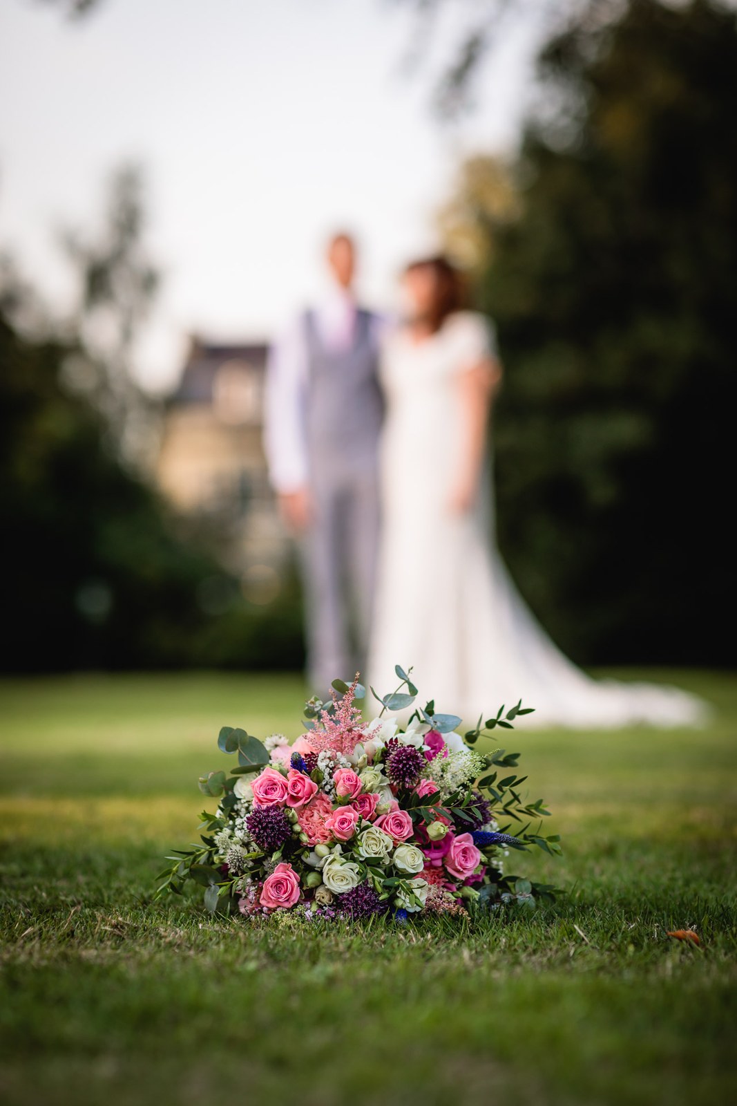 The bouquet resting on the grass with the couple blurred behind at dusk