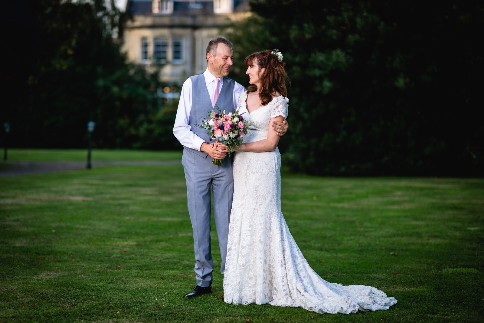 Bride and groom embracing on the lawn at golden hour, the hotel behind
