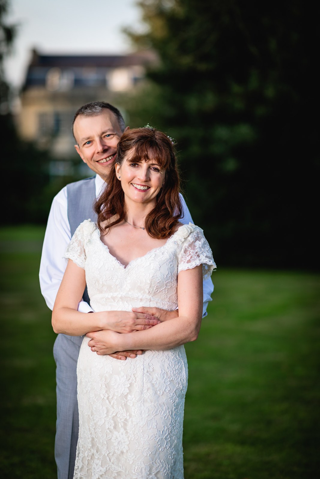 Groom holding the bride from behind on the lawn at sunset
