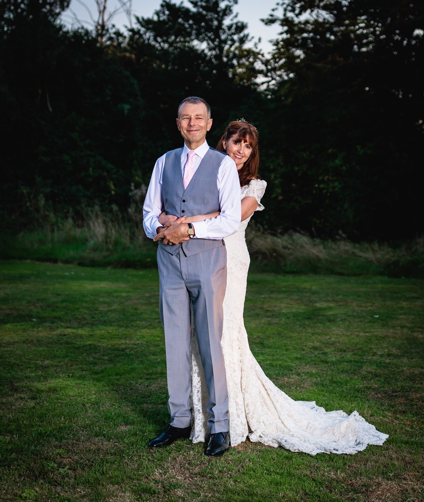 The couple embracing on the lawn at dusk, the bride's train trailing