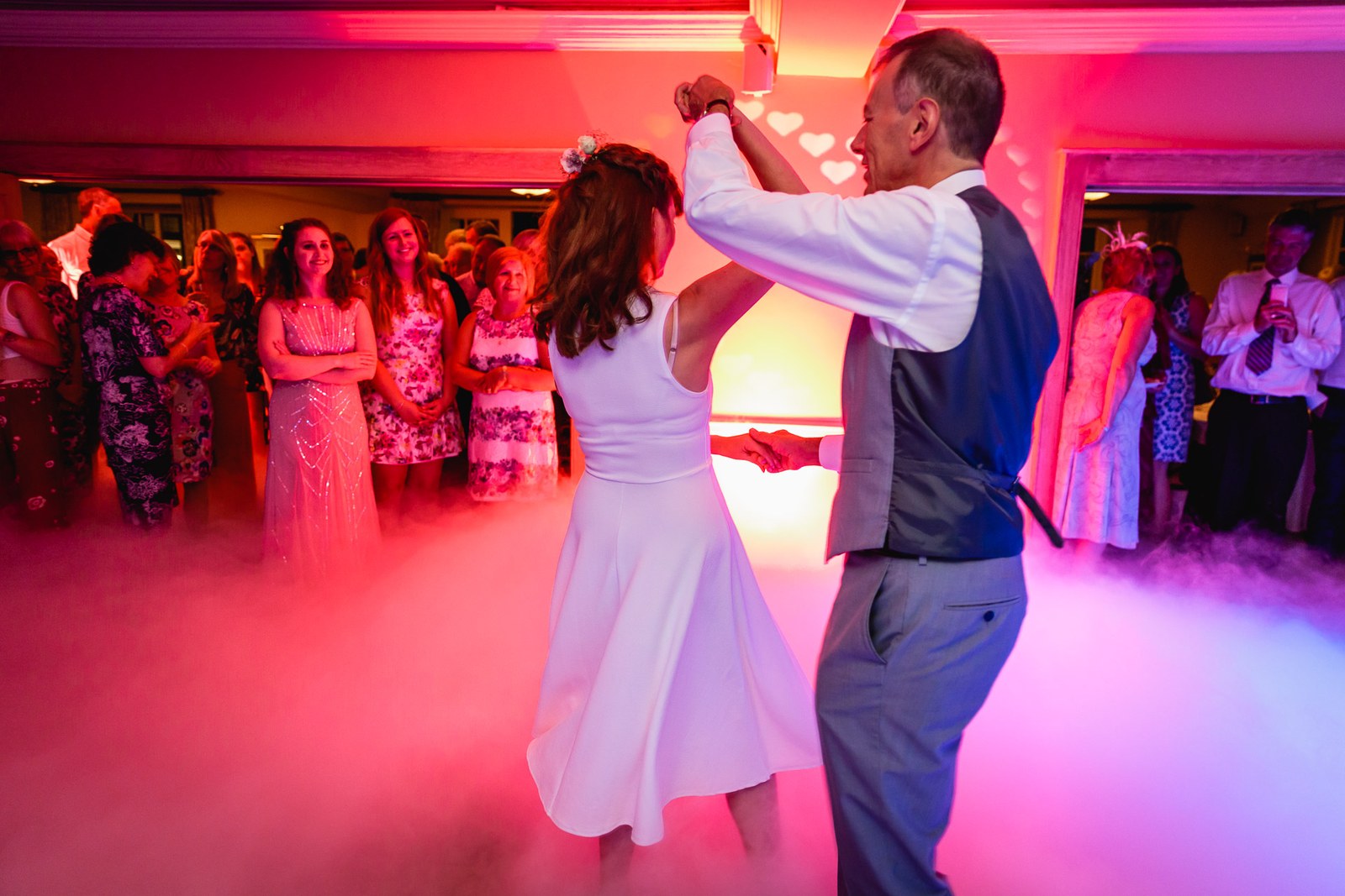 Bride and groom's first dance amid coloured lighting and smoke as guests watch