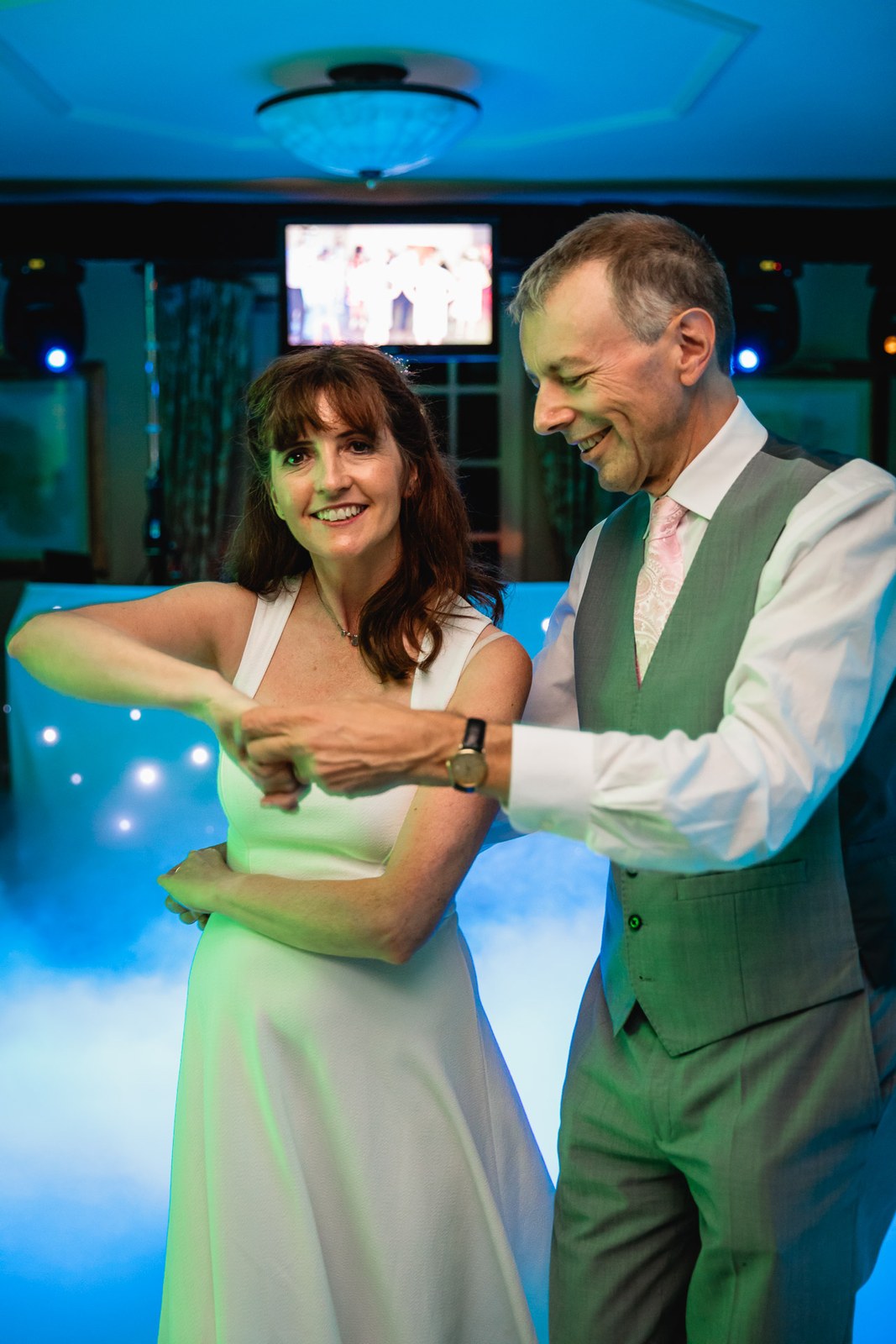 Bride and groom dancing in swirling dry-ice smoke under blue light