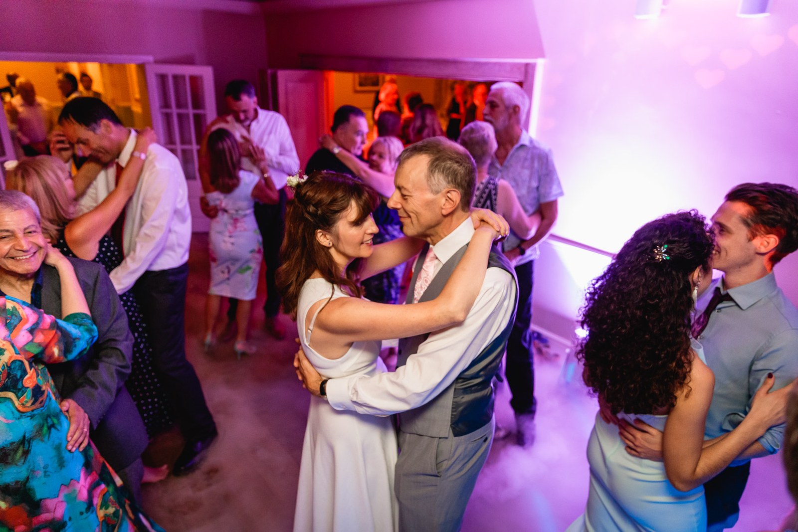 The couple and guests dancing together on a busy floor under pink lighting