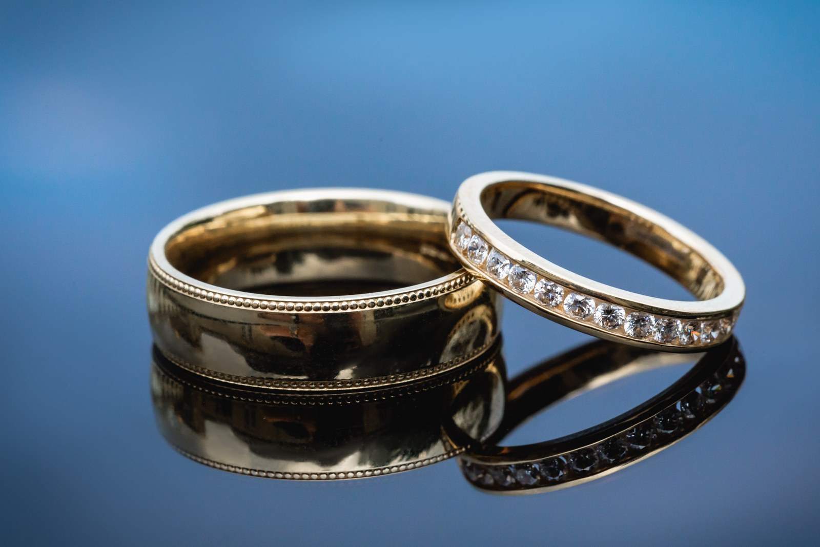 Close-up of two gold wedding rings, one diamond-set, on a blue surface