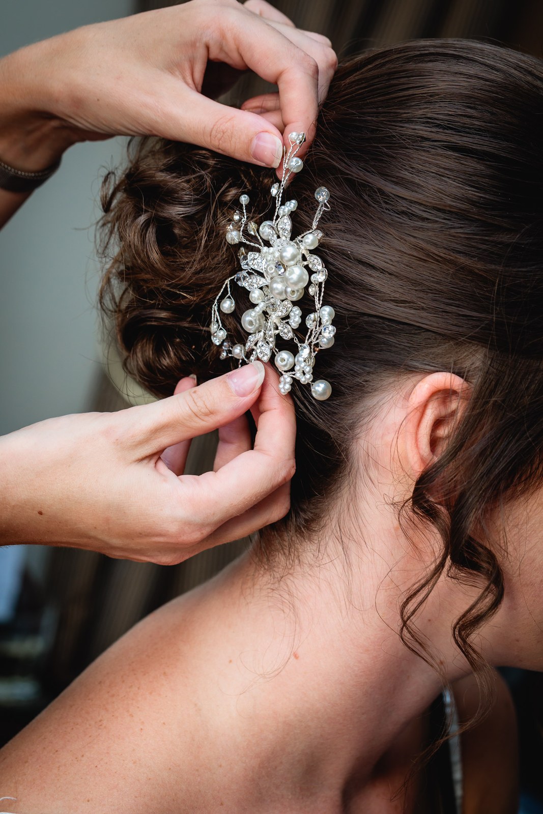 Hands fixing a pearl and crystal comb into the bride's dark updo