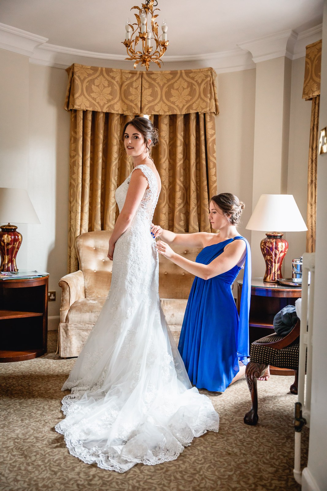 Bride having her gown laced up by a bridesmaid in a suite at Macdonald Berystede Hotel