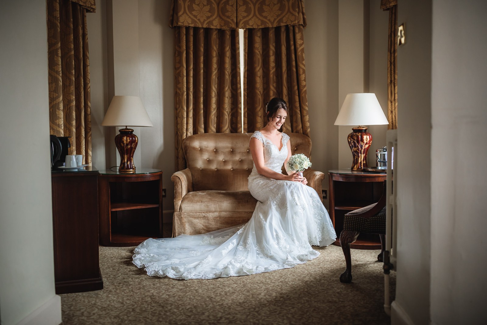 Bride seated on a gold buttoned sofa holding her bouquet in the hotel suite