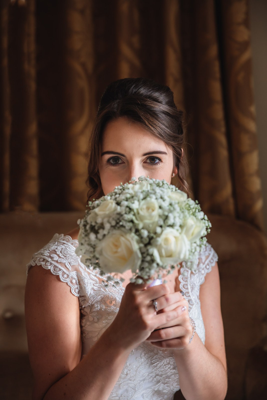 Bride holding a white rose and gypsophila bouquet up to her face