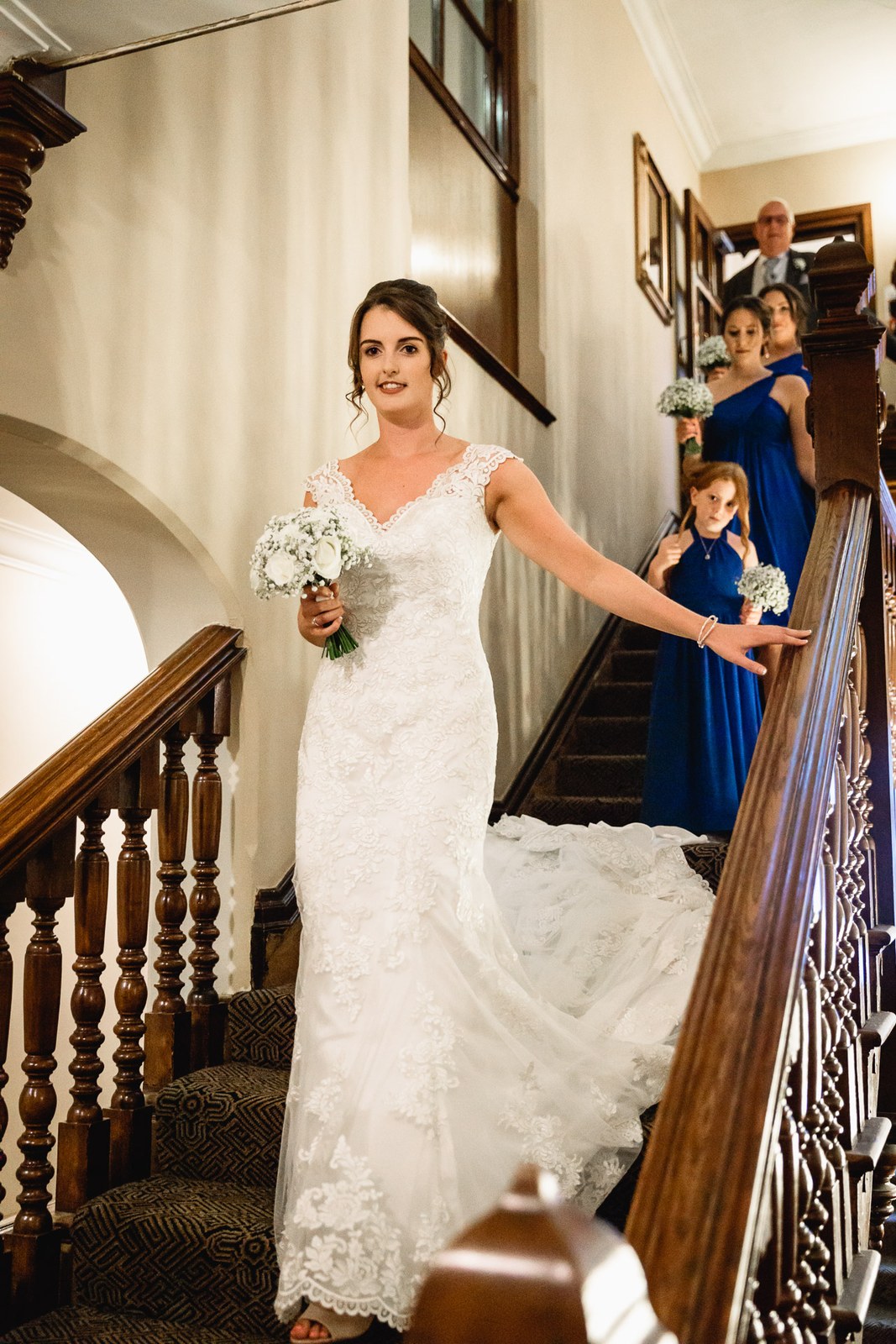 Bride descending the grand wooden staircase of Macdonald Berystede Hotel, bridesmaids behind