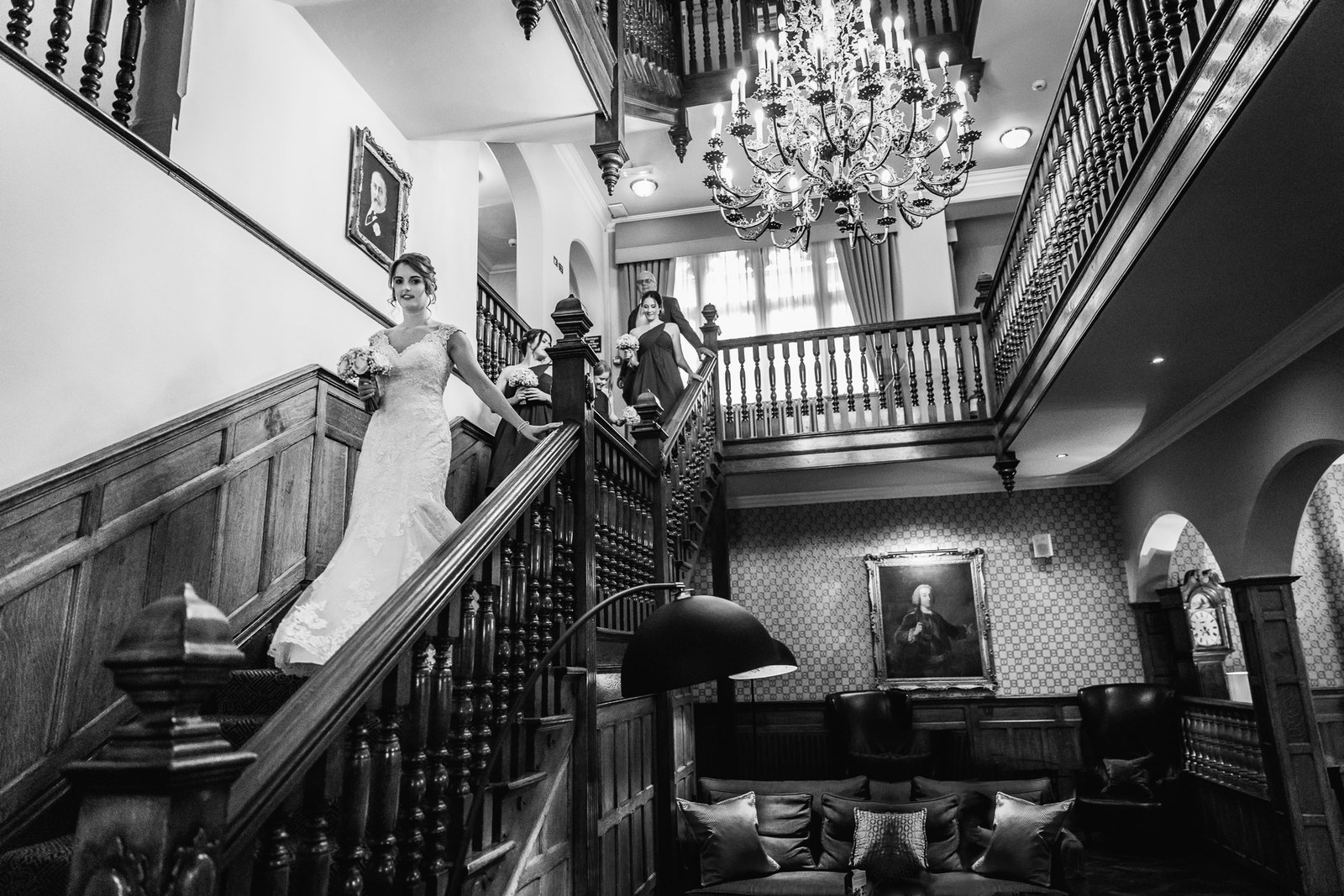 Black and white view of the bride on the hotel's panelled staircase beneath a chandelier