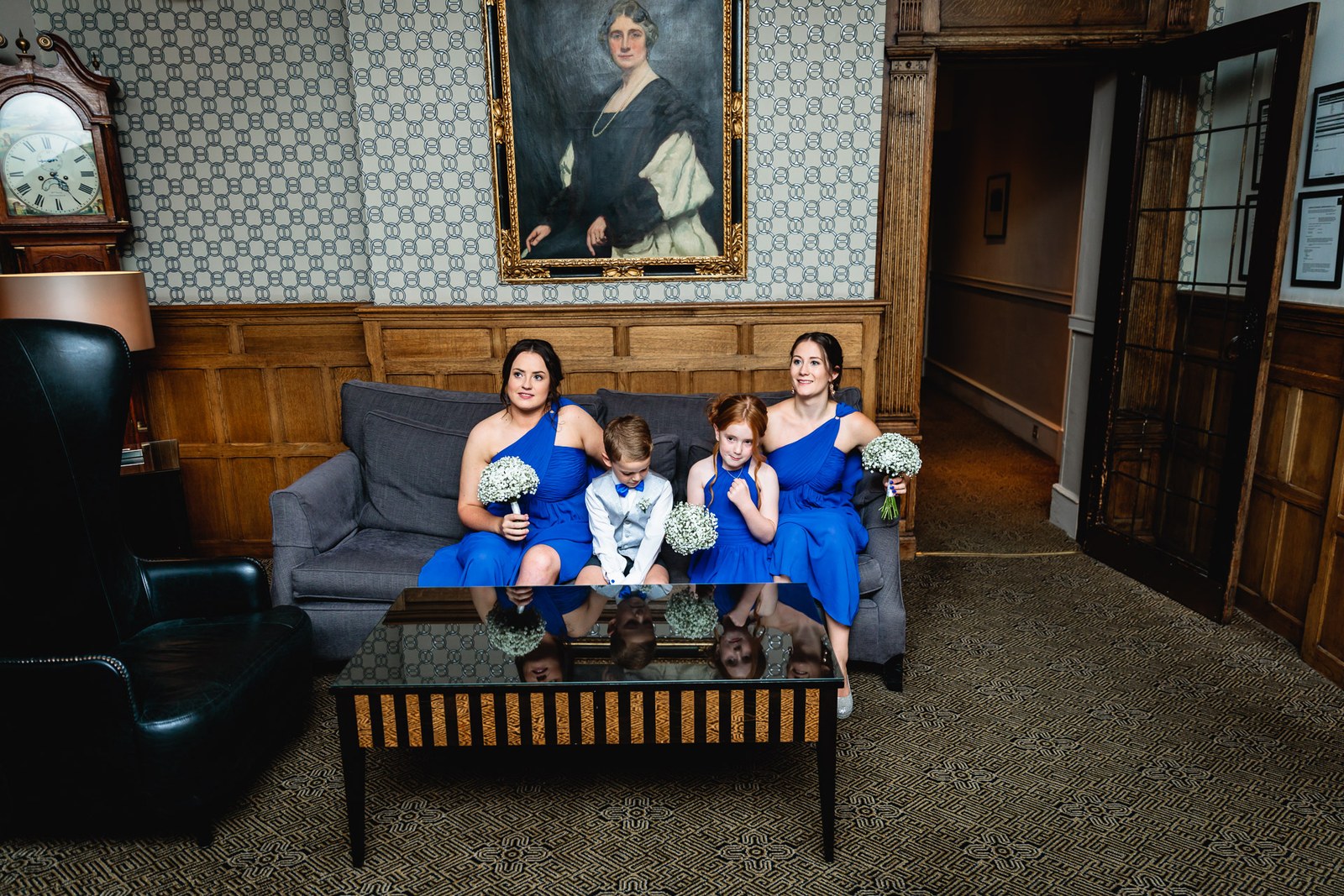 Bridesmaids and a page boy on a sofa in a wood-panelled room with an oil portrait