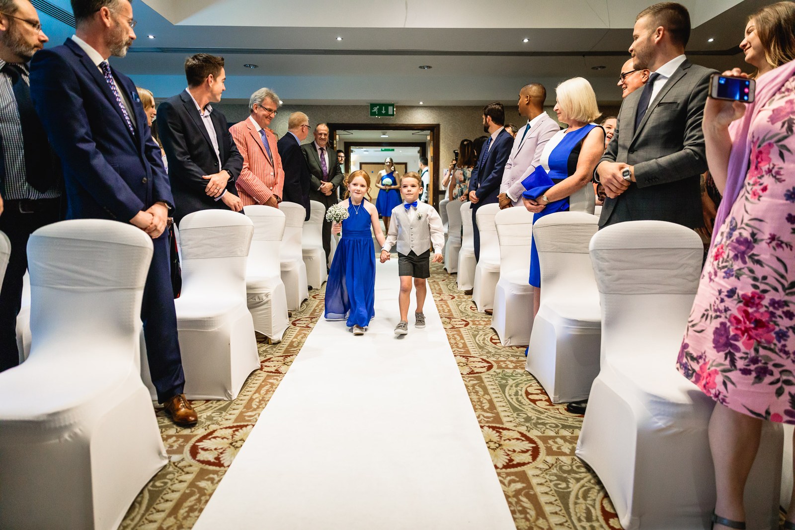Flower girl and page boy walking down the aisle as guests stand