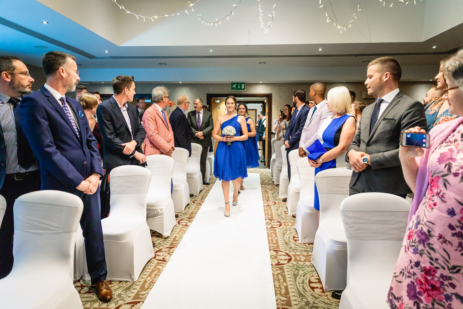 A bridesmaid walking the white-carpet aisle as standing guests watch