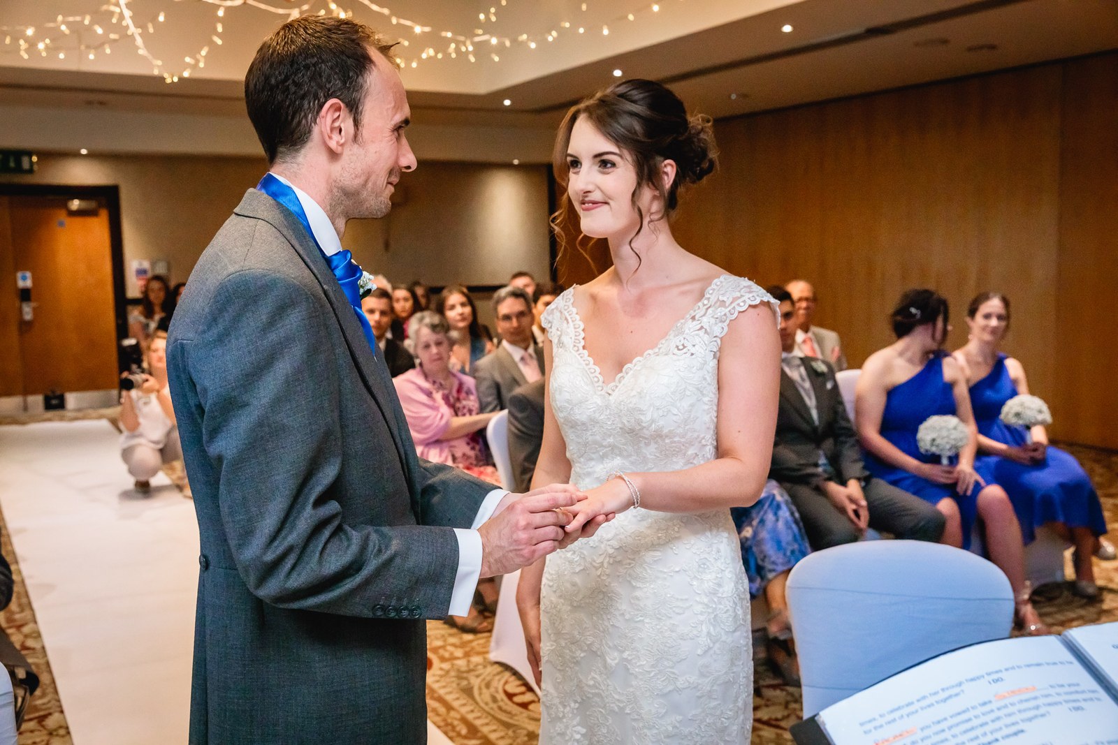 Bride and groom facing each other exchanging rings, guests seated behind