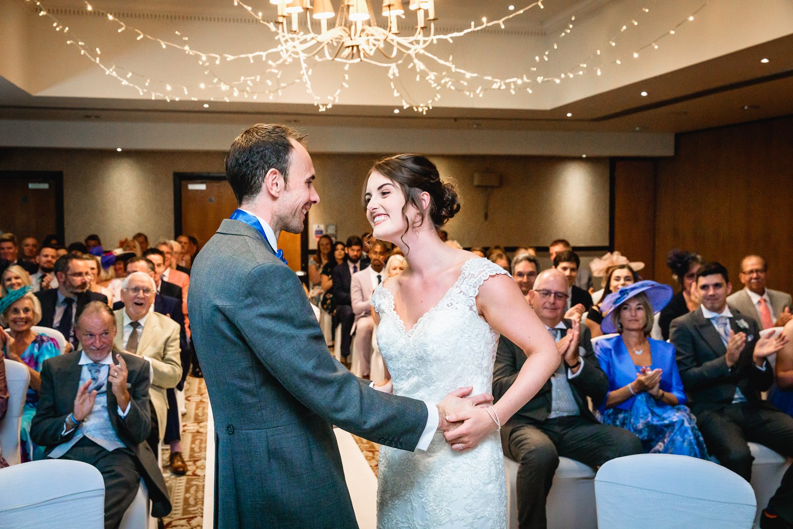The couple holding hands and beaming at each other as guests clap