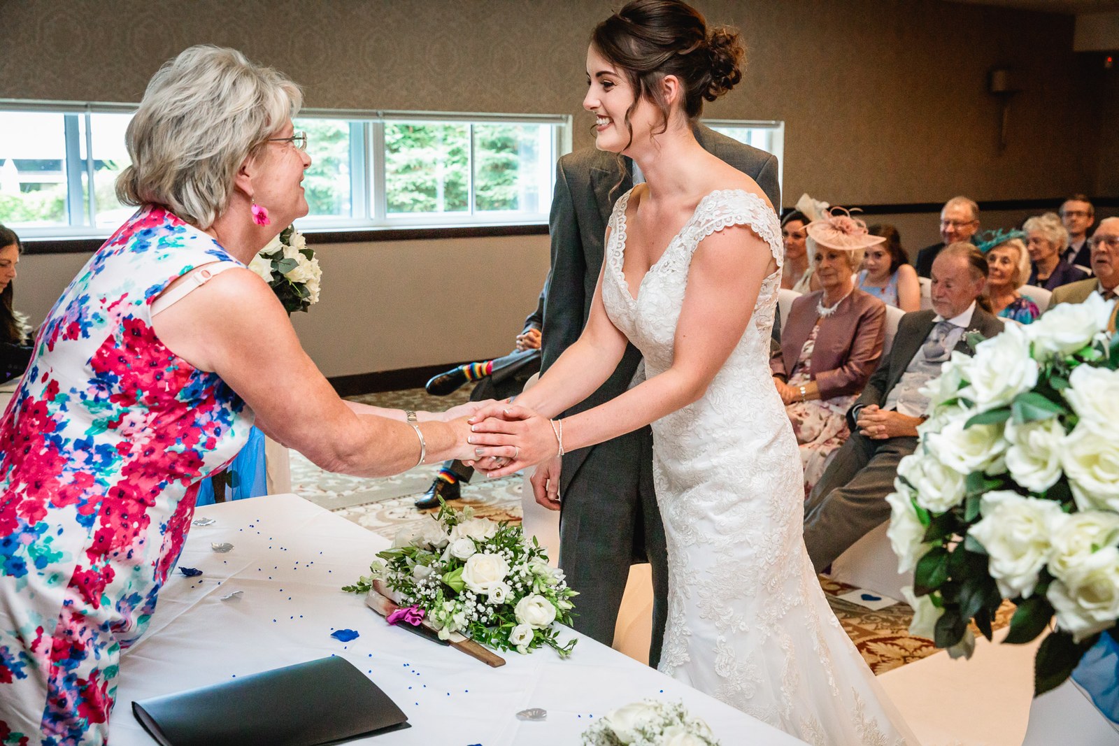 Bride greeting the registrar in a floral dress at the signing table