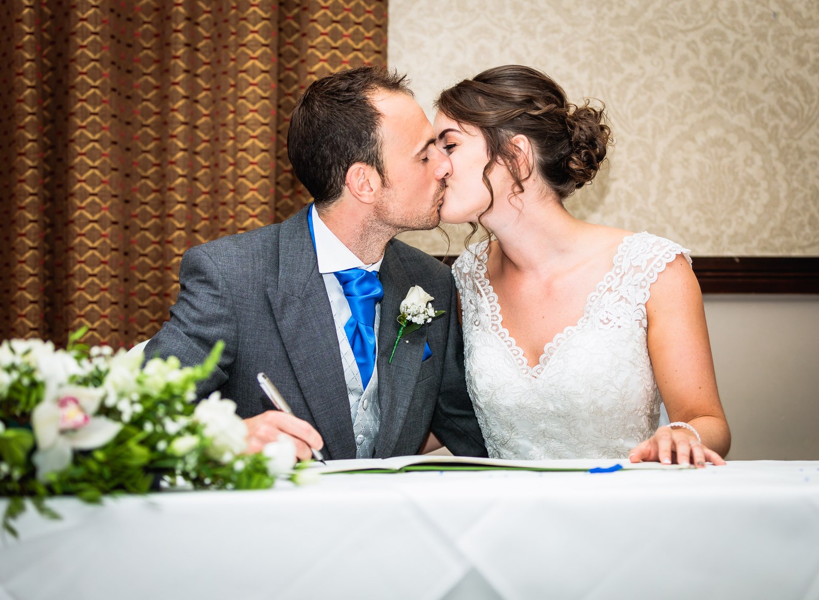 Bride and groom kissing at the signing table beside the register and flowers