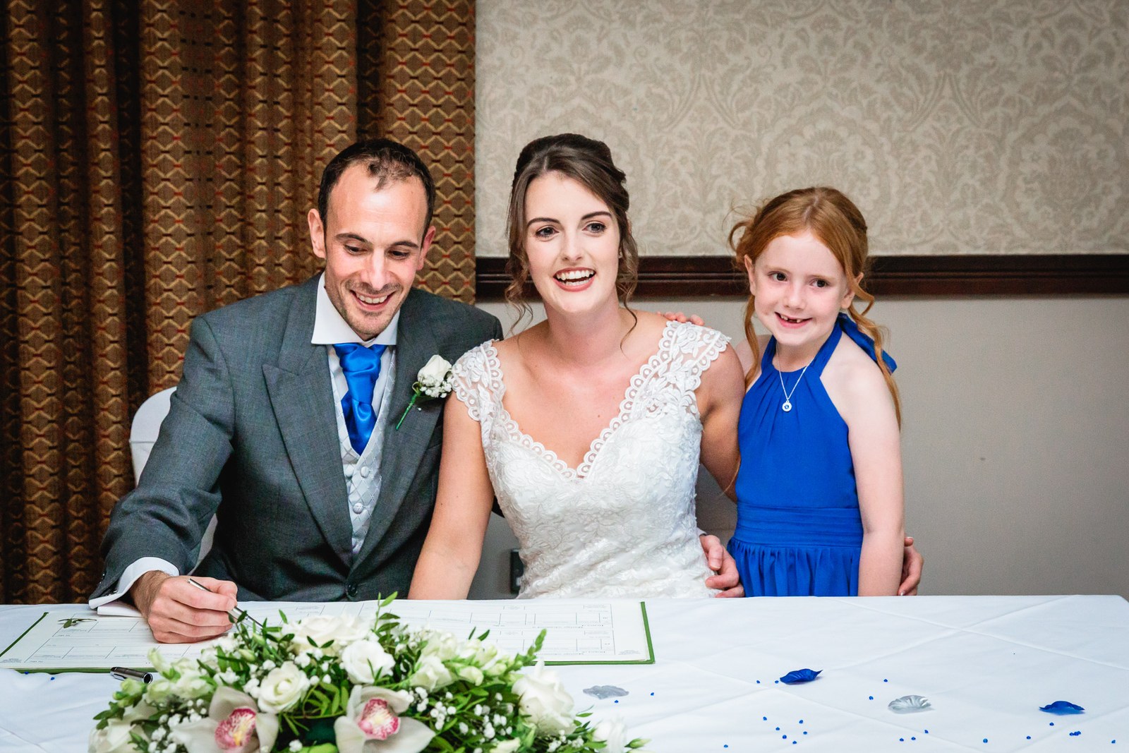 Bride and groom posing with a flower girl at the signing table