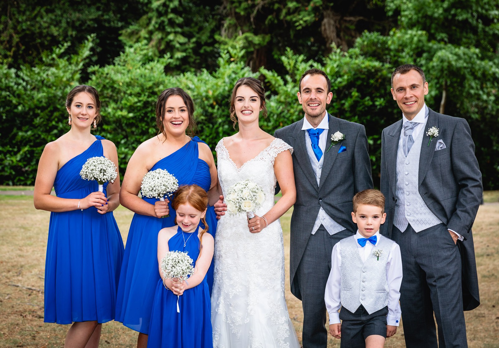 Bride and groom with bridesmaids in blue, a flower girl, page boy and a groomsman