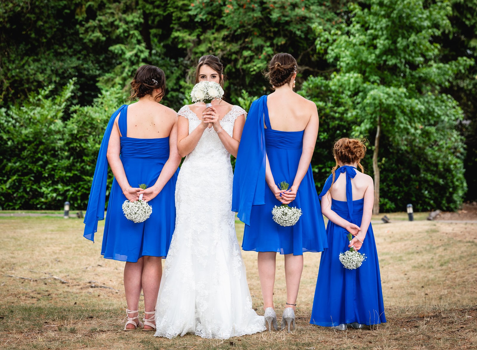 Bride hiding her face behind her bouquet, bridesmaids gathered around