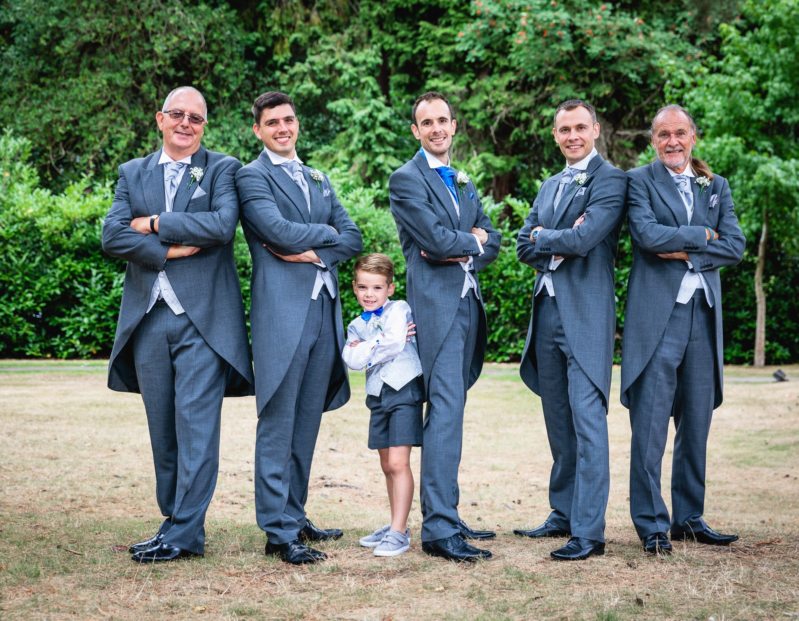 Groom and groomsmen in morning suits, arms folded, a page boy between them