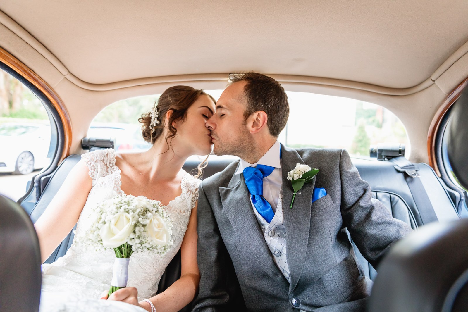 Bride and groom kissing in the back seat of the car, bouquet on her lap