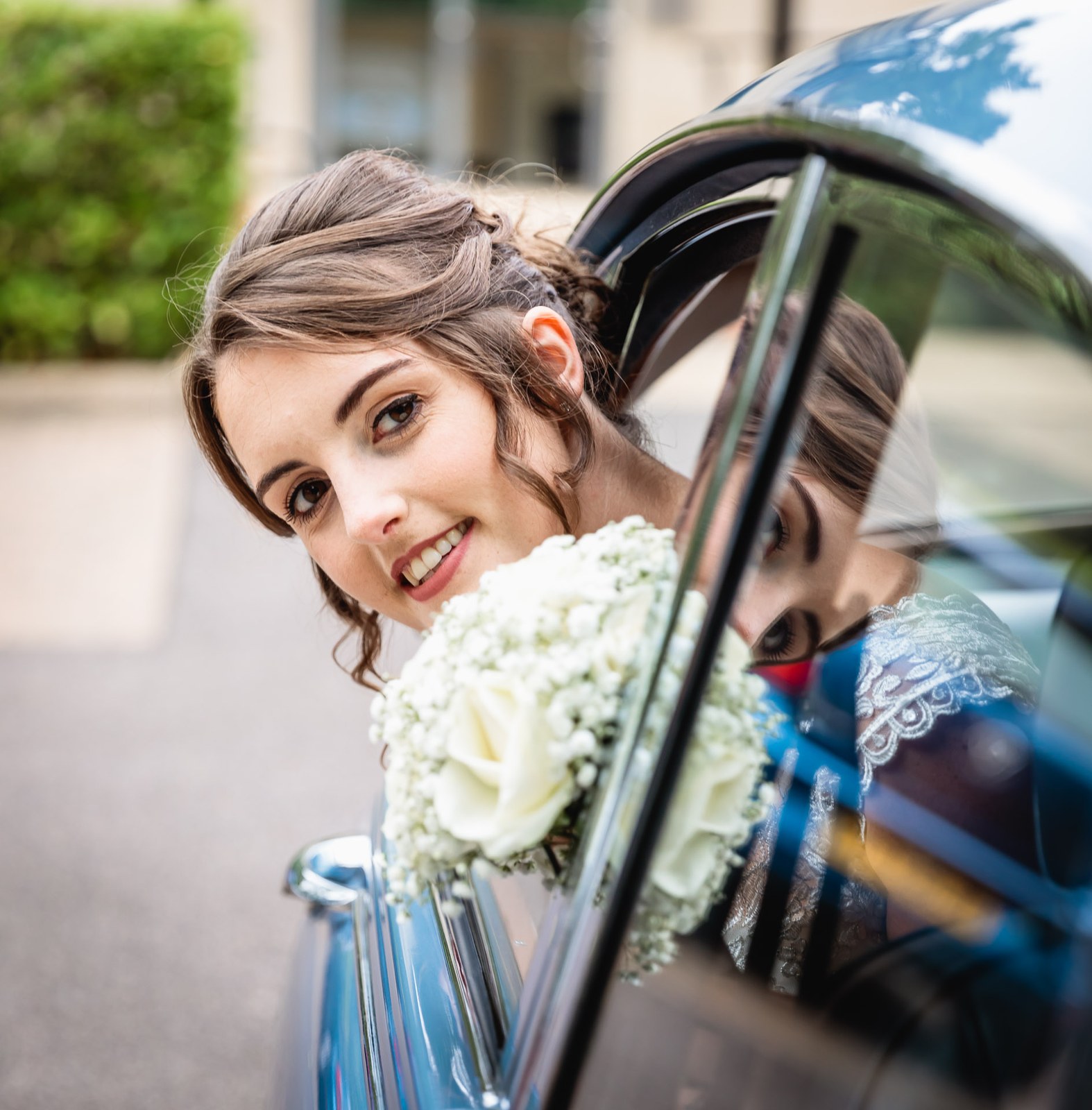 Bride leaning from the car window with her white rose bouquet