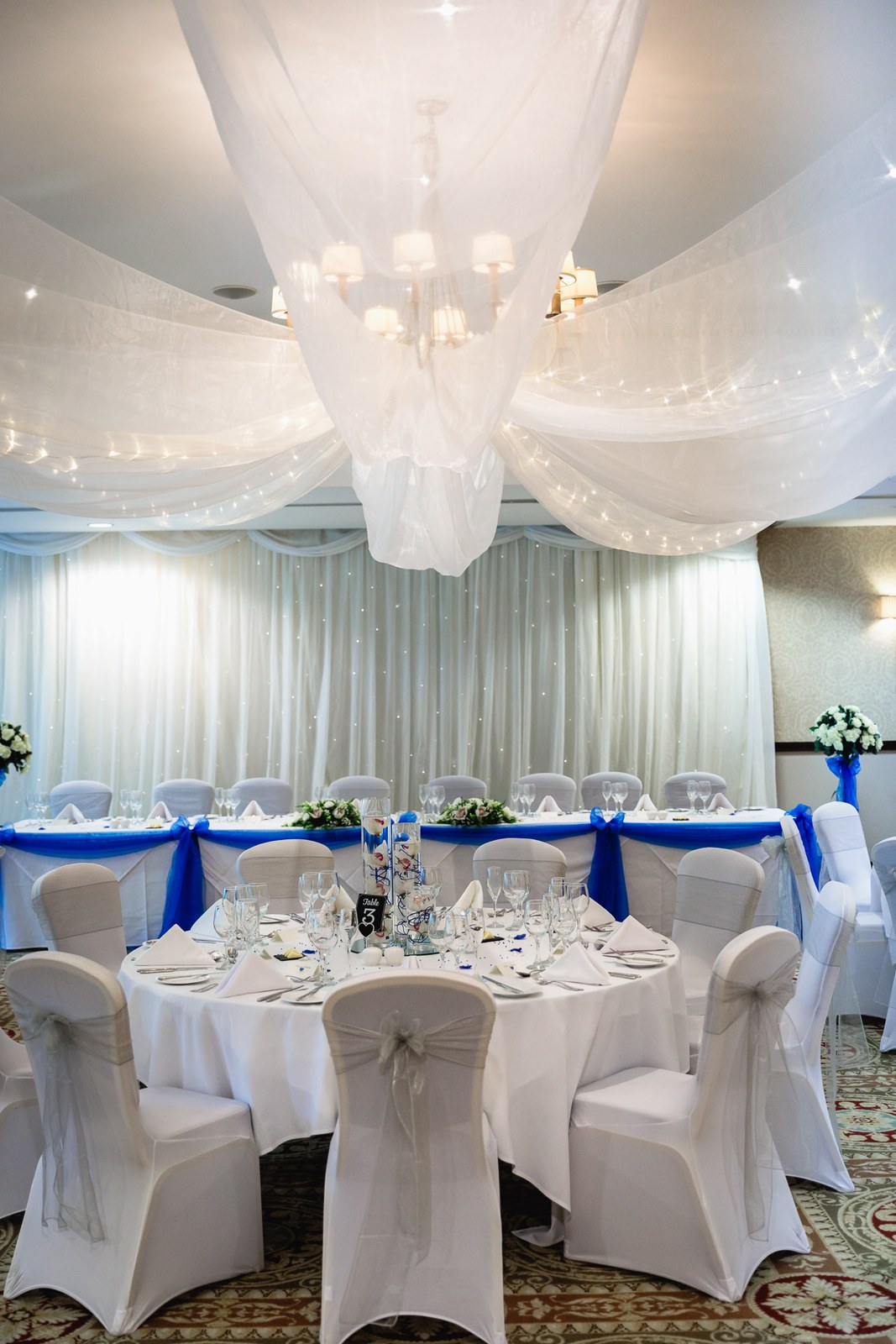 The reception room at Macdonald Berystede Hotel with a draped ceiling and blue-sashed tables