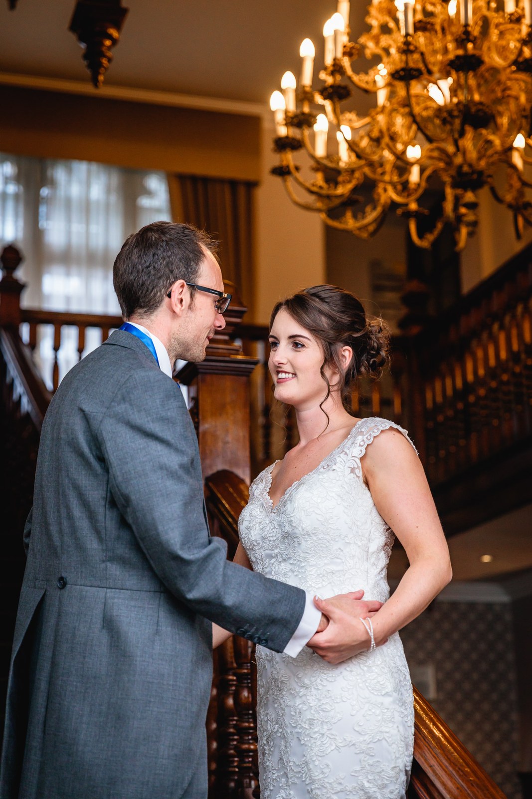 Bride and groom embracing beneath a golden chandelier at Macdonald Berystede Hotel