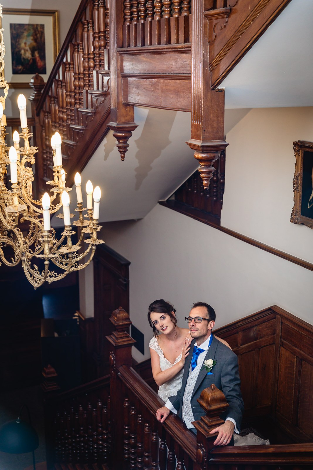 The couple on the hotel's grand wooden staircase below an ornate gilt chandelier
