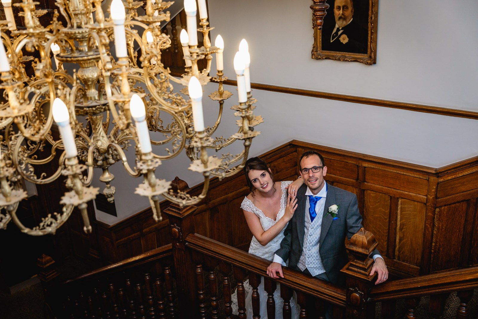 Bride and groom leaning on the staircase banister under a gold chandelier and portrait
