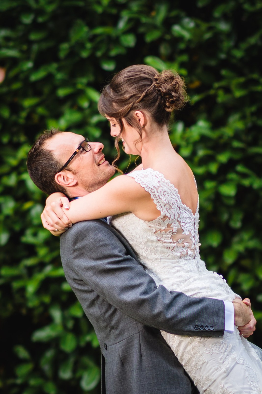 Groom lifting the laughing bride beside a leafy hedge