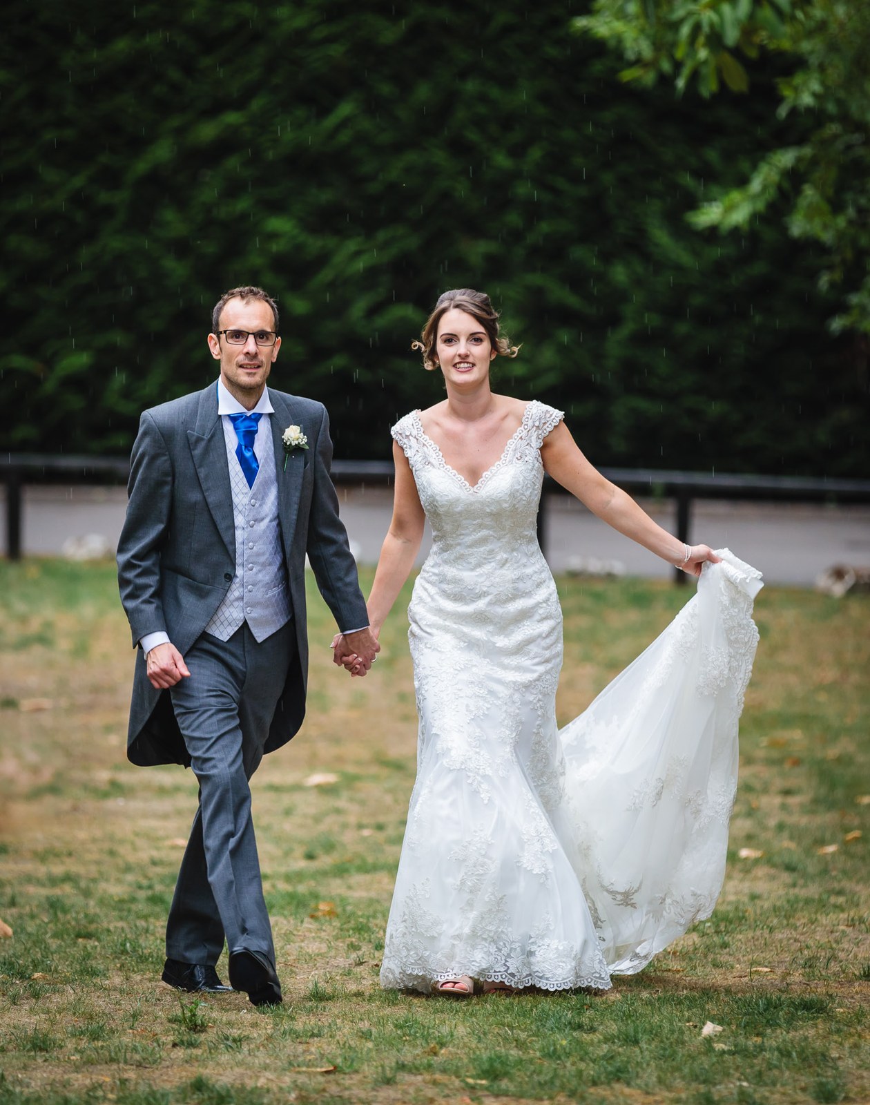 Bride holding out her train as she walks with the groom through the grounds