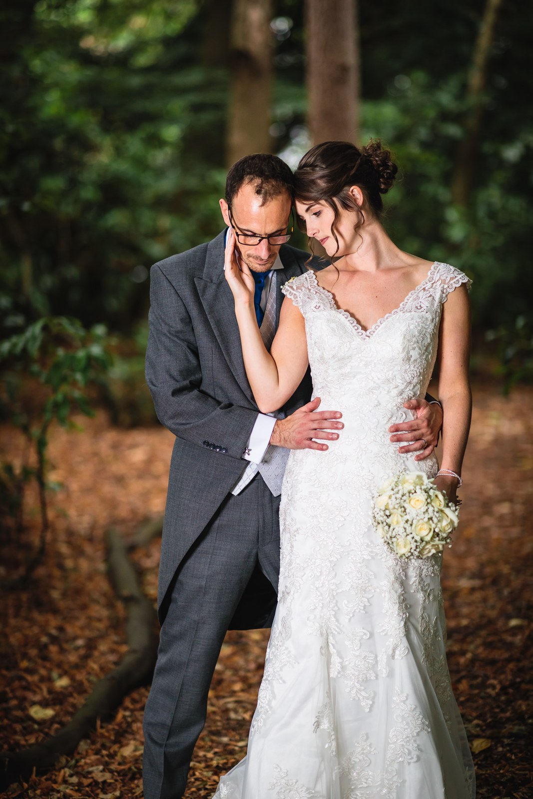 Bride and groom embracing among the woodland trees, bouquet in hand