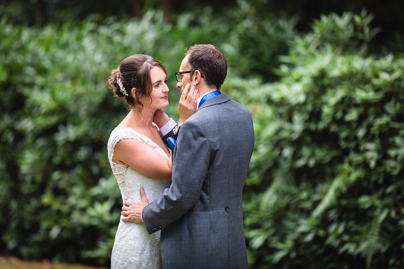 The couple embracing by a green hedge, the bride cupping the groom's face