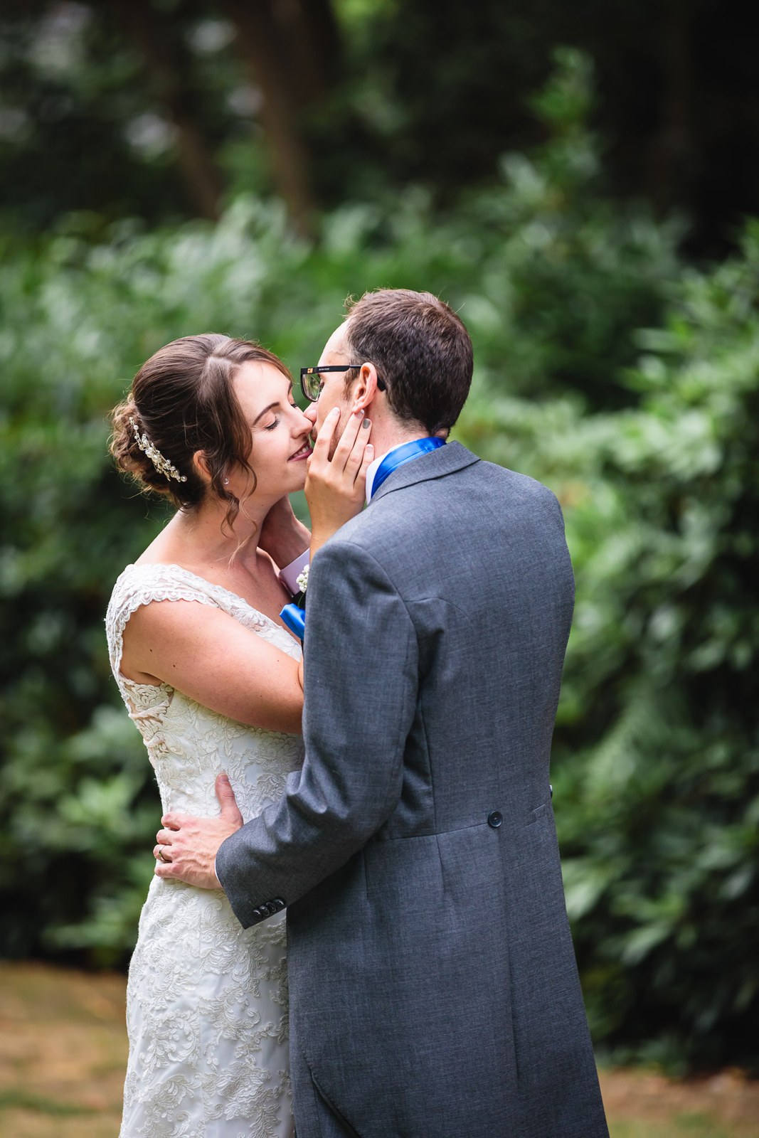 Bride and groom about to kiss beside a leafy hedge