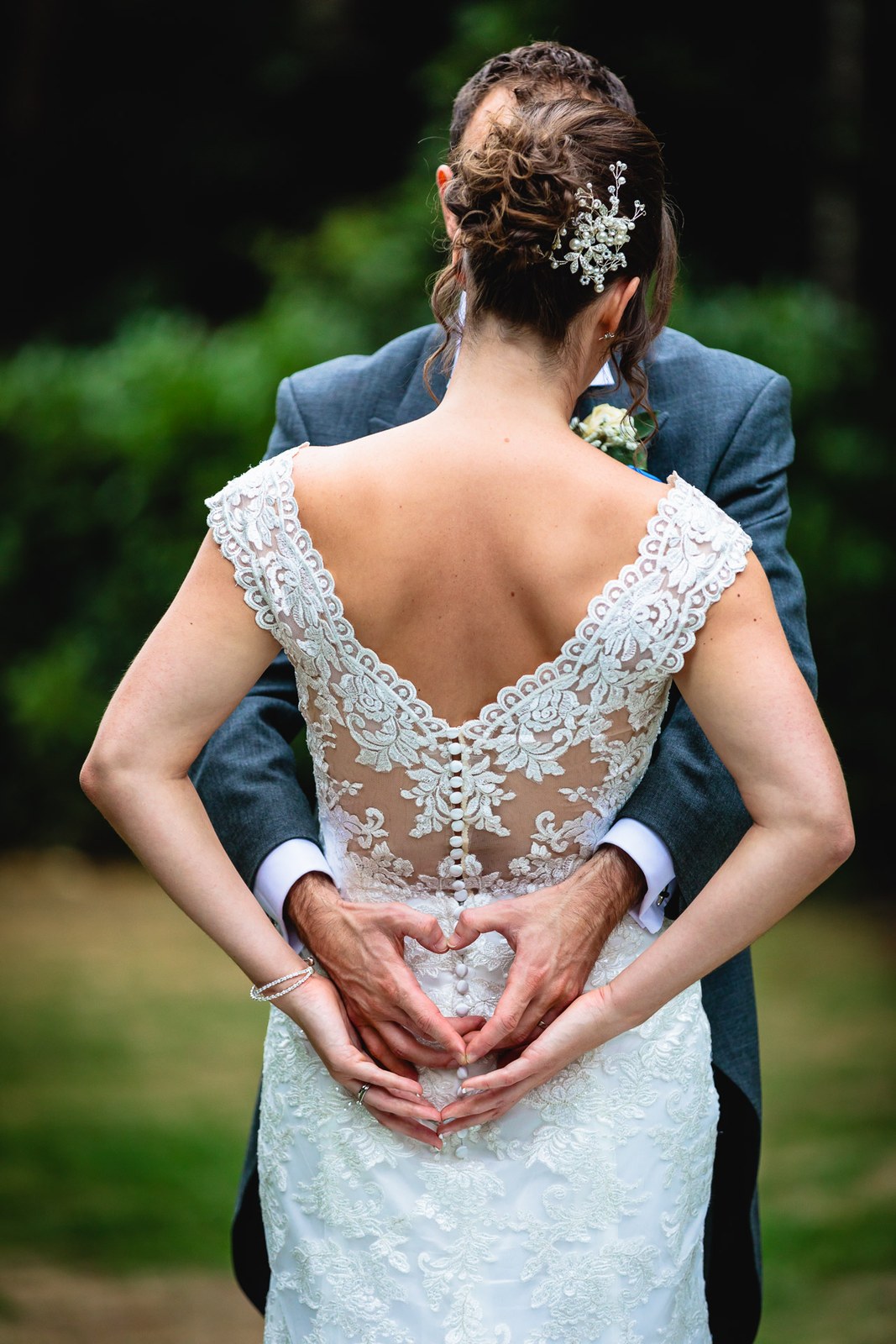 Bride from behind showing the lace button back of her gown, hands forming a heart