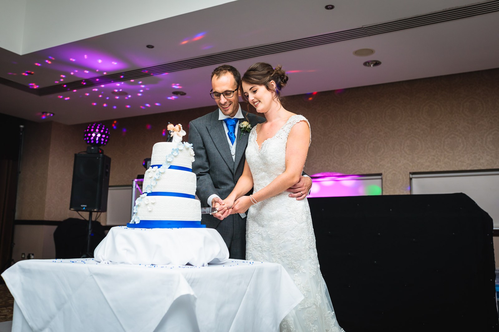 Bride and groom cutting their cake under purple lighting by the dance floor