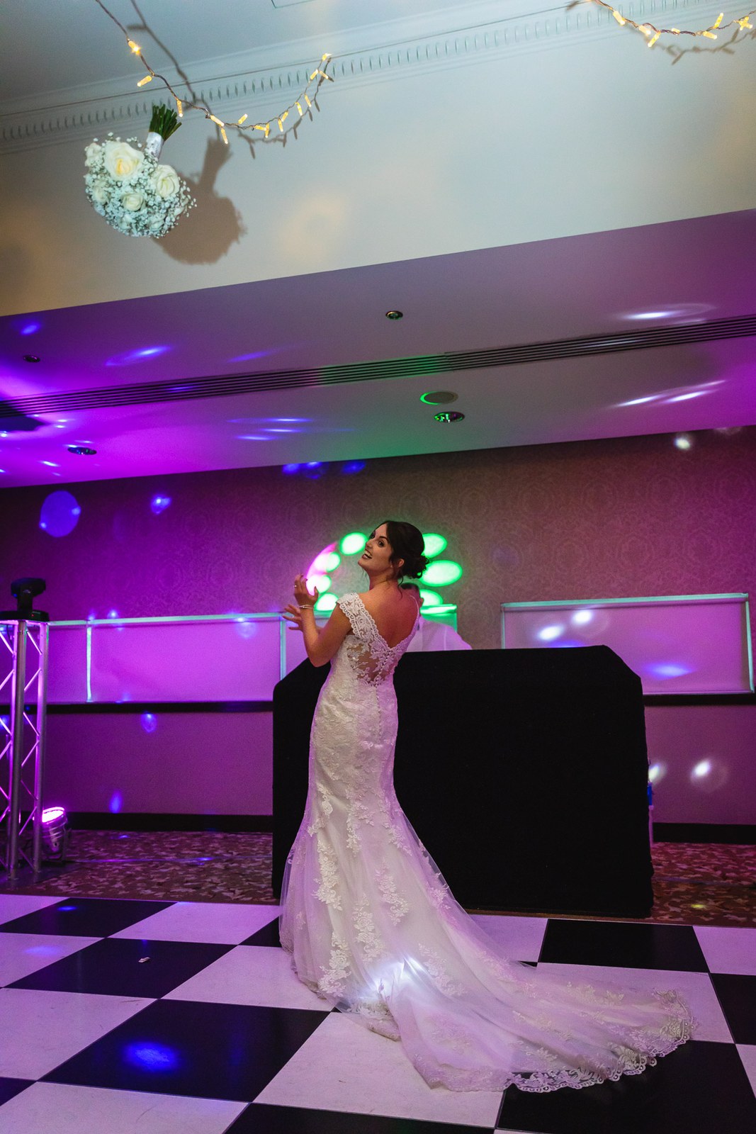 Bride throwing her bouquet on the chequered dance floor under purple lighting