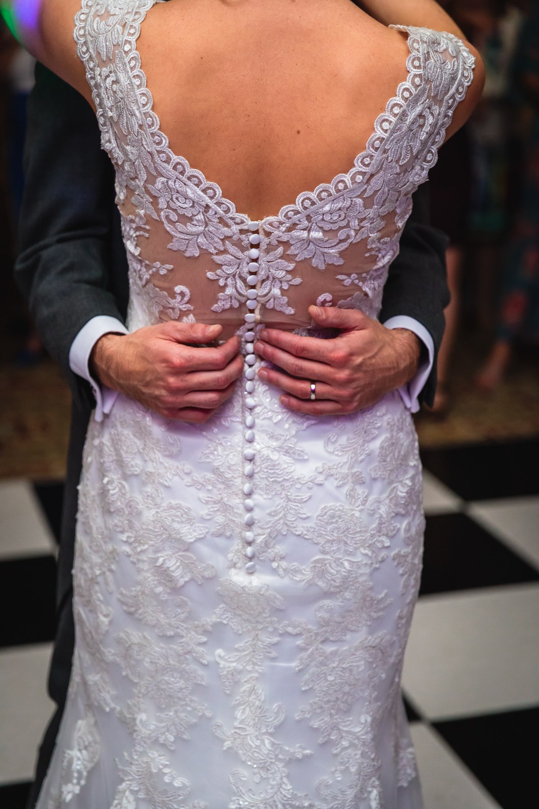 Bride from behind on the chequered dance floor, the groom's hands at her laced back