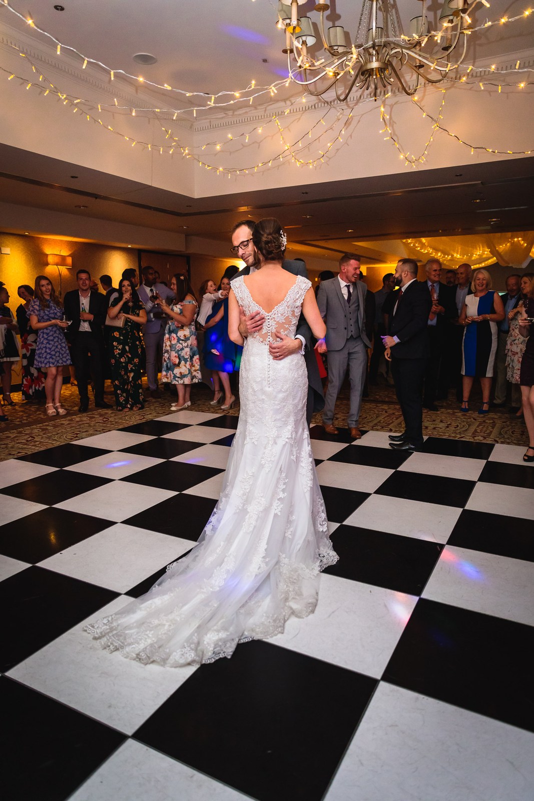 Bride from behind on the chequered dance floor beneath fairy lights and a chandelier