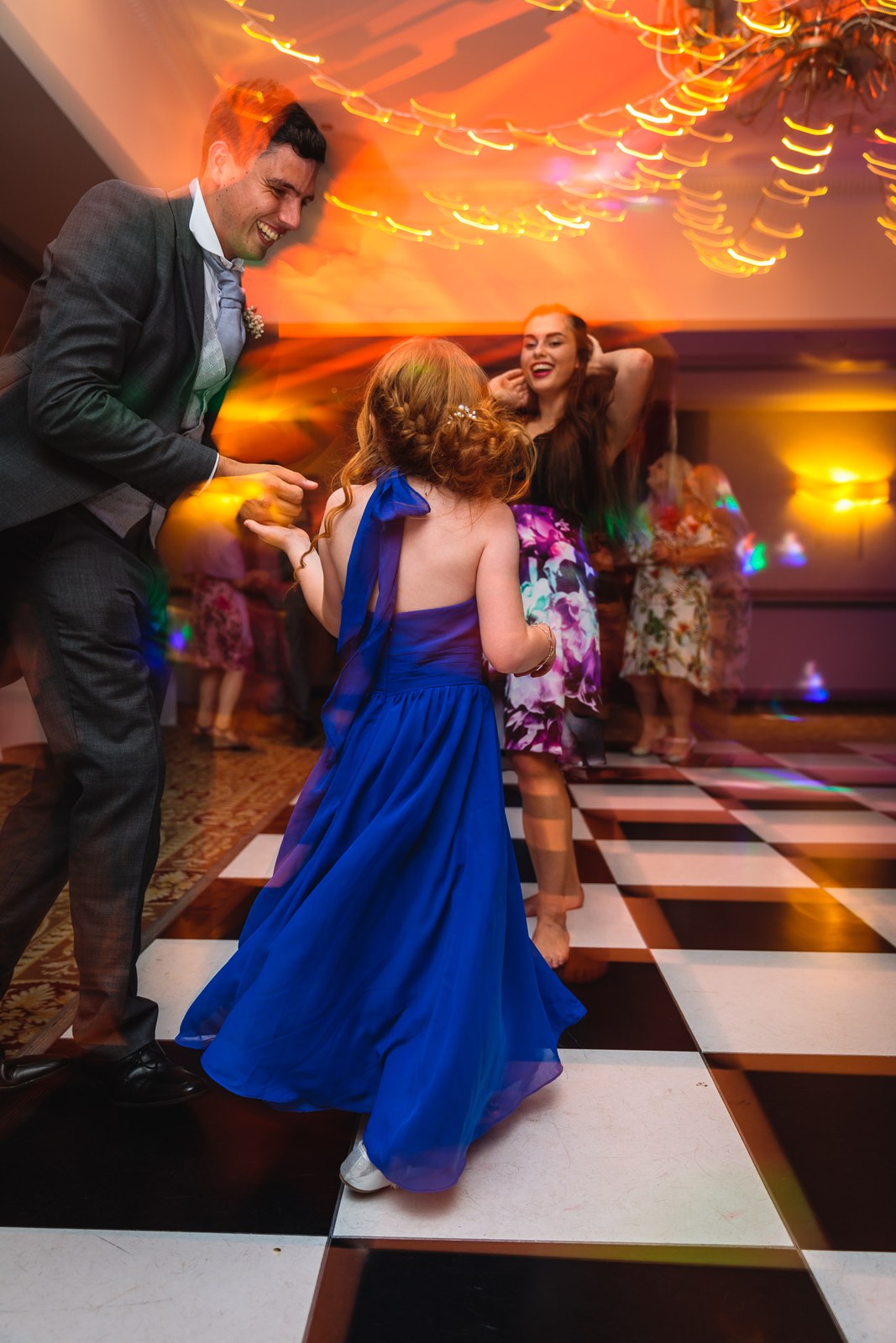 A groomsman dancing with the flower girl in blue on the chequered floor